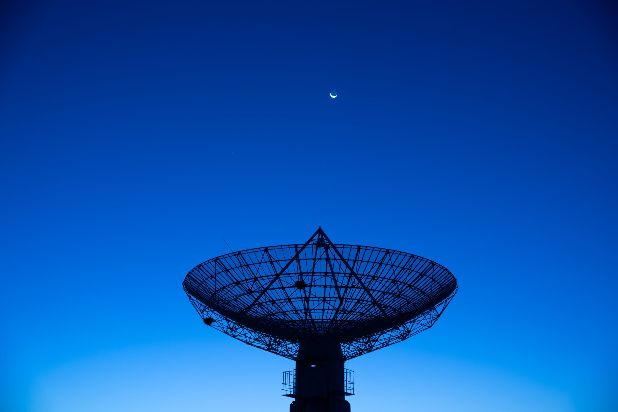 Satellite dish under crescent moon at dusk.