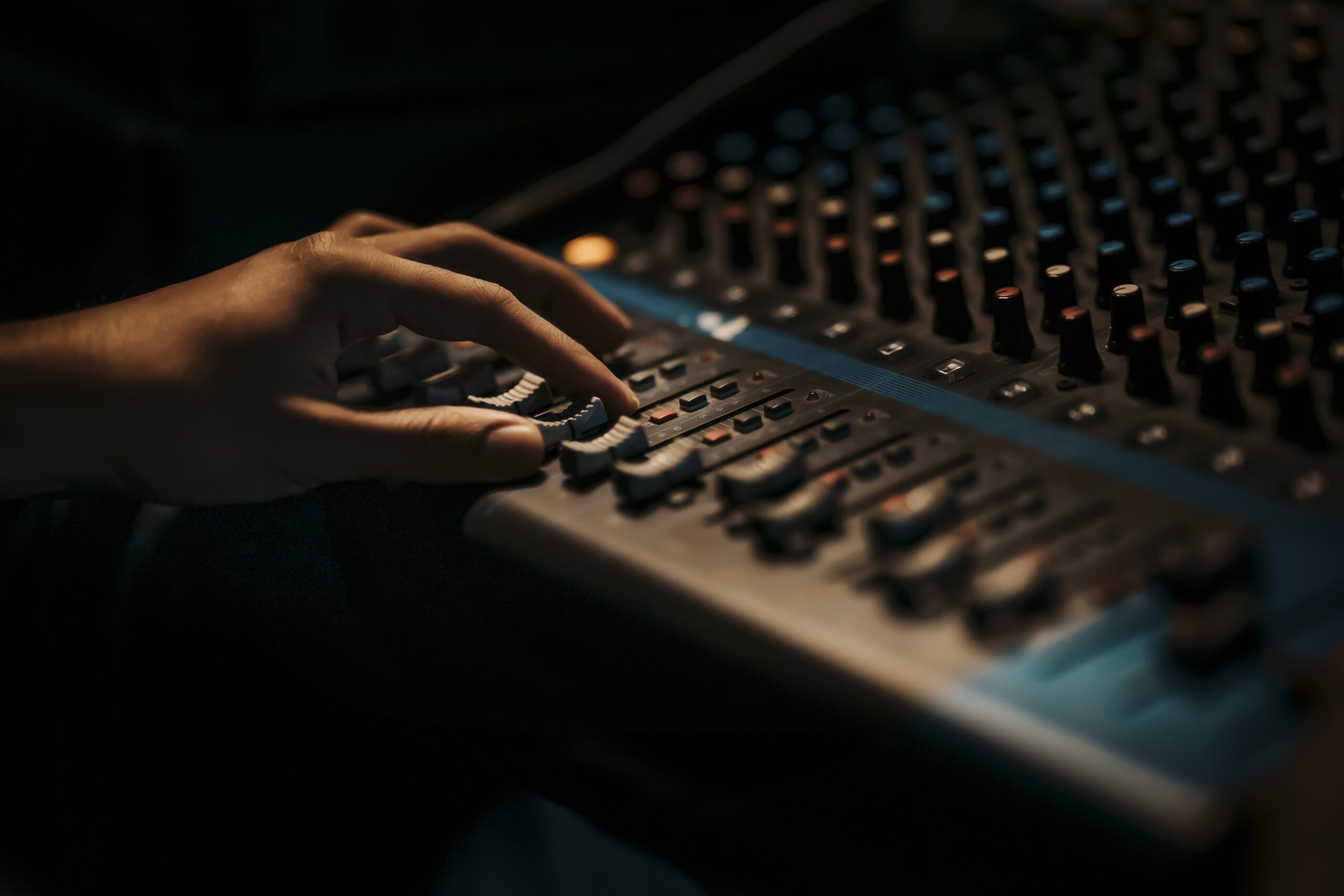 Hand adjusting audio mixing console sliders.
