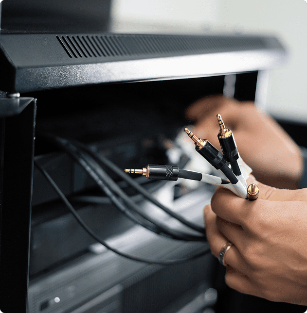 Hand holding various audio cables near equipment.